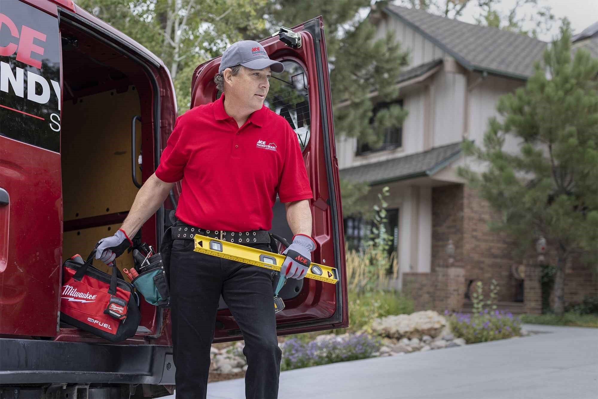 An Ace Handyman professional grabbing his tool bag and a leveler from the back of his van before he heads in for a project.