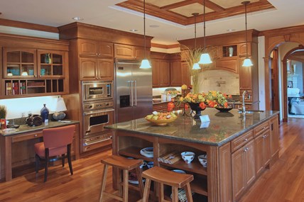 A large, luxurious kitchen with wood cabinets, a stone countertop on a central island, and three pendant lights hanging above. A large, luxurious kitchen with wood cabinets, a stone countertop on a central island, and three pendant lights hanging above.