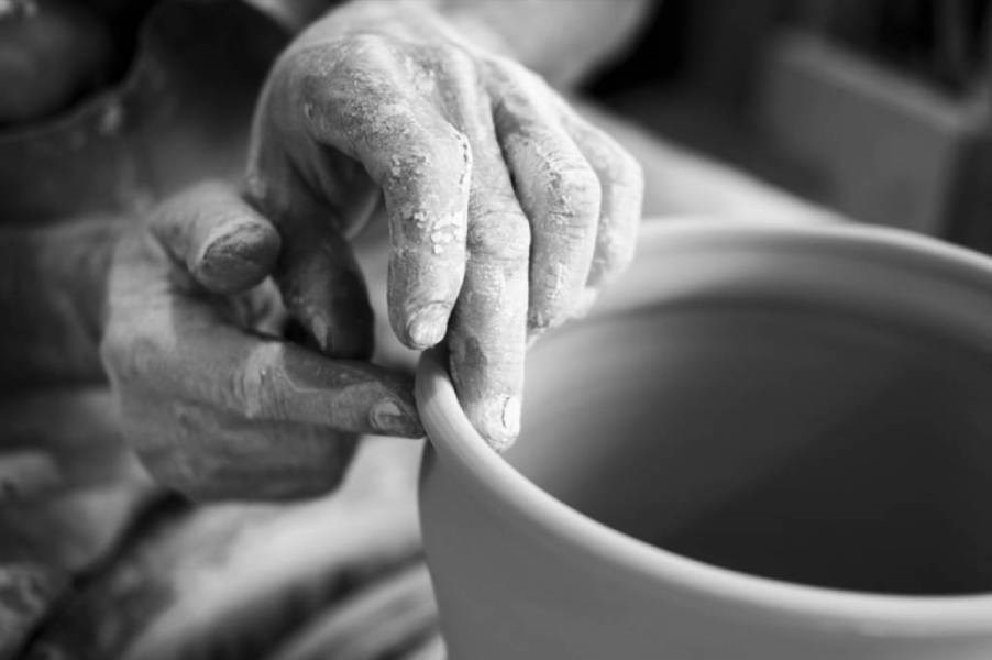 Black and white photo of someone using their hands to shape a bowl on a pottery wheel