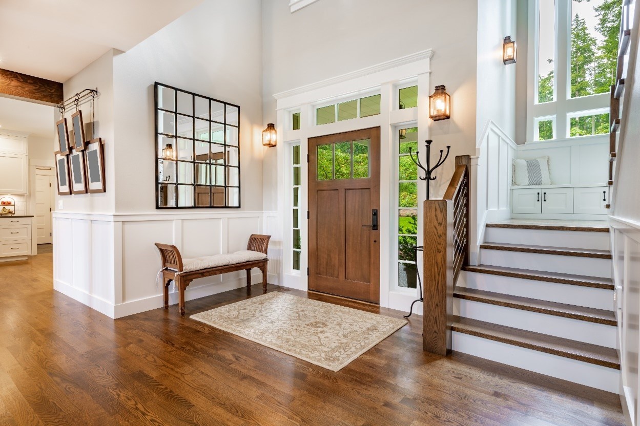 Interior front entry with a brown door and windows around it, mirror on the left and staircase on the right with window above