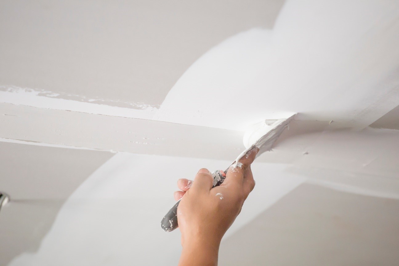A hand holding a putty knife to apply putty to drywall
