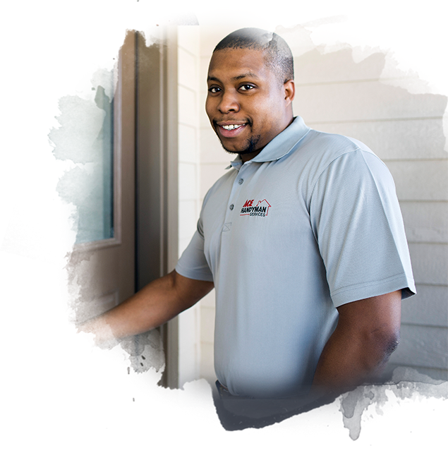 A smiling man in a gray Ace Handyman Services polo reaching one arm out to a door next to him. A smiling man in a gray Ace Handyman Services polo reaching one arm out to a door next to him.