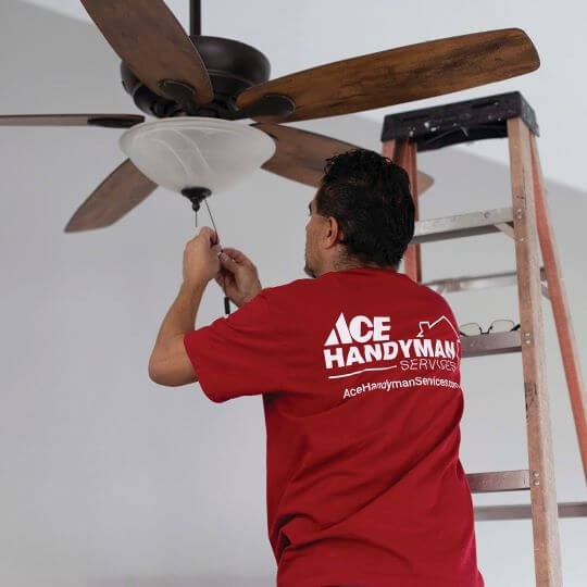 A handyman installing a fan into the ceiling of a house A handyman installing a fan into the ceiling of a house