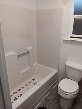 Bathtub enclosure with damage to the rim and alphabet stickers on the floor of the tub, The tub appears to be smooth fiberglass. 