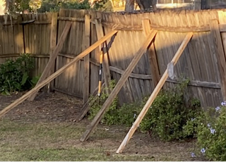 Leaning wooden fence supported by temporary 2x4 braces, showing signs of weather damage and unstable posts in residential backyard.