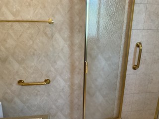 Bathroom with two newly installed gold grab bars matching the gold shower door and towel rod, providing added safety and a coordinated look.