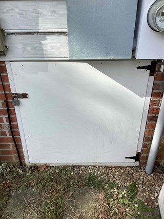 The same crawlspace door, now with a repaired or replaced lower edge. The door is painted smooth, and the padlock remains in place.