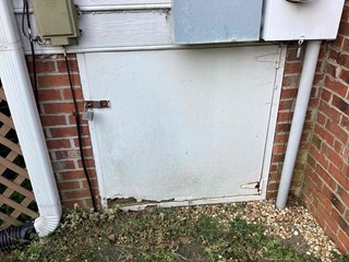 A crawlspace door with visible damage near the bottom edge. The white door has some peeling and exposed wood on the lower part, and the door is secured with a padlock.