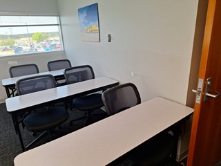 A classroom with a light-colored wall and several chairs and desks. The wall shows some minor damage with scuff marks near the corner from the chairs hitting it. 