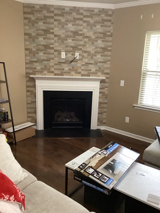 A living room with a beige-colored wall and a fireplace. The fireplace has a white mantel, and the wall above is decorated with stone-like tiles. 