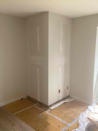 The same room, now with the wall fully constructed and drywalled. The corner is smooth, and the surface appears freshly finished with some drywall tape visible. 