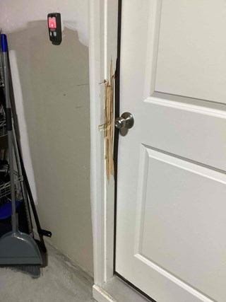 A close-up of a white door with significant damage on the left side of the door frame. The doorframe is split, with pieces of the wood coming apart.