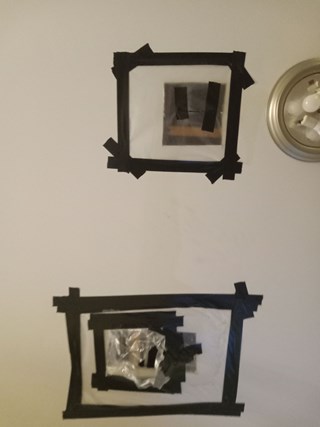 A close-up of a ceiling featuring two rectangular openings covered by black tape and plastic sheeting. One of the openings has a few pieces of black tape, while the other is taped more thoroughly with overlapping black tape and plastic.