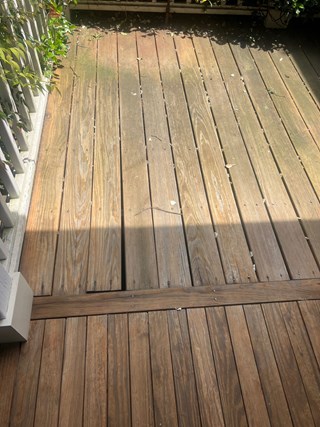 Wooden deck that is weathered and worn, with noticeable discoloration and wood rot in some areas.