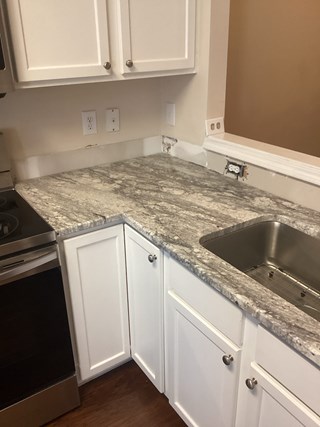 Kitchen countertop with a partially finished backsplash area. The countertop and cabinetry are in place, but the area above the counter, where the backsplash should be, is unfinished, with exposed wall space and electrical outlets visible.