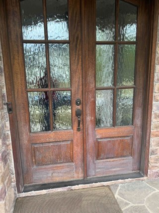 Entry door with noticeable wear on its wooden surface. The door has visible scratches and discoloration, giving it an aged and weathered look. The wooden frame and panels are slightly faded, and the door appears in need of refinishing or repainting.