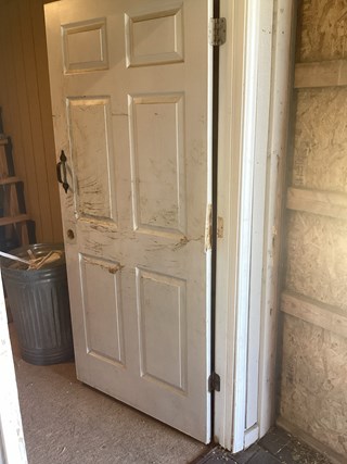White door with visible damage. The surface is scratched and marked, with the door frame also appearing worn.