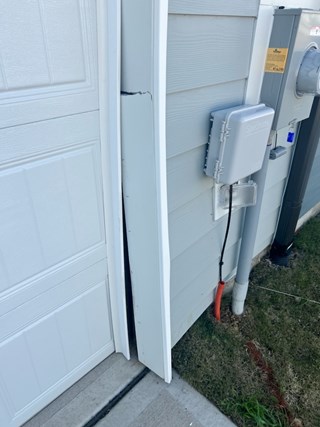 Exterior of a garage with visible damage to the trim around the garage door. There is a noticeable gap or misalignment between the trim pieces, and the trim itself appears cracked or bent.
