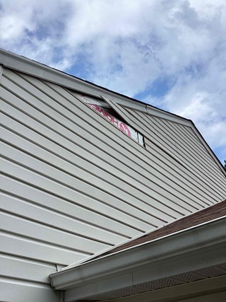 Home's exterior with damaged vinyl siding. There is a large gap of exposed area at the top where a piece of siding is missing, revealing the underlying structure.