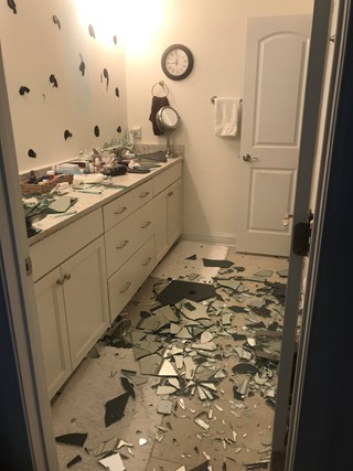 Bathroom after a mirror has fallen off with a significant amount of shattered glass on the floor. 