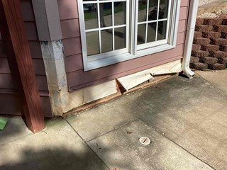 Section of the home's siding with visible damage near the base of the wall, under the window. 