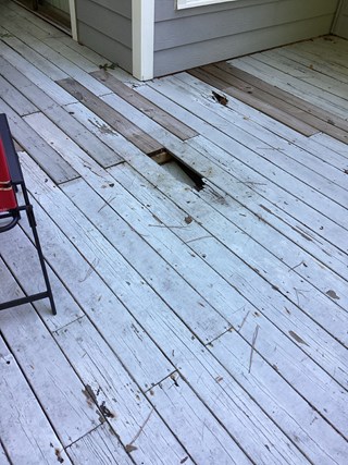 The deck has a visible large hole in the wood, with sections of damaged or weathered boards scattered around the area. The surface appears uneven and worn down.
