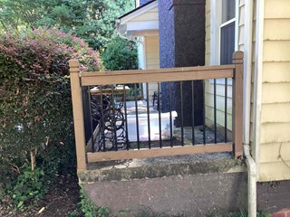 Wooden railing with black metal spindles on a small platform or porch. The railing appears to be in good condition, though the wood has some signs of wear, and the black paint on the metal spindles is slightly faded.