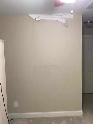 Wall with peeling paint and damage, including visible water stains and a section where the drywall is exposed.