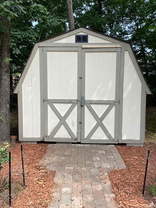 Wooden shed with double doors that are showing signs of water damage and deterioration around the framing. 