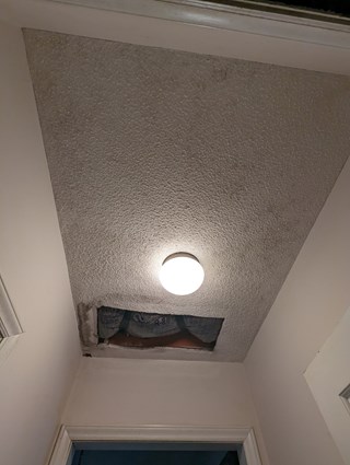 Ceiling with a large hole around a light fixture, revealing the insulation behind it. The ceiling appears to have some water damage