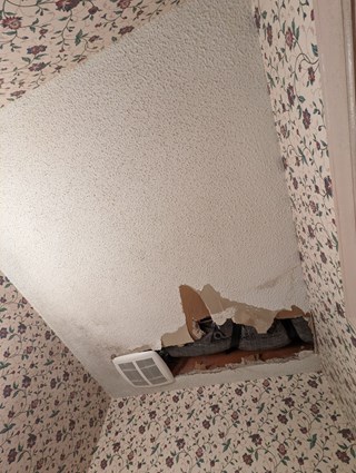 Significant damage to a ceiling, with a large section of drywall missing around a vent. 
