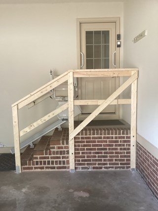 Stairs with a newly added wooden railing installed along the side of the stairlift. The railing is still in its raw, unfinished form, with wooden posts and diagonal bracing, offering added stability and safety for users.