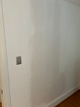 Wall after drywall repair work. The drywall has been patched, and the wall has been primed, although it may still require a final coat of paint for a smooth finish. 