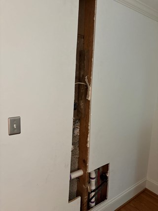 Section of drywall that has been cut open, revealing plumbing behind it.