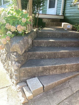Concrete steps are damaged, with cracks and uneven surfaces. Additionally, the area at the base has loose stones or bricks, which could be a safety hazard.