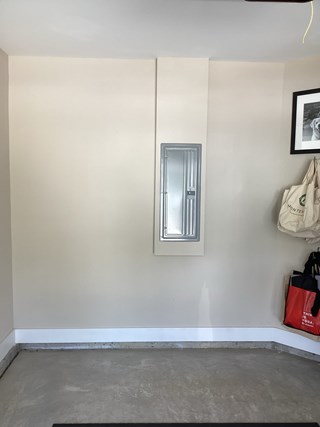 A garage wall with an electrical panel in the middle of the wall. 