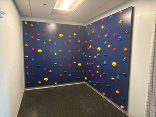The wooden slats are covered with a smooth, dark-colored surface, and various brightly colored climbing holds have been installed, turning the wall into a functional climbing surface. The room is now ready for use as a climbing space.