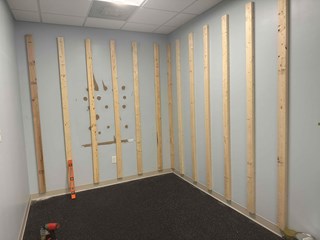Unfinished walls with wooden slats installed, as the framework for the climbing wall at a commercial facility. 