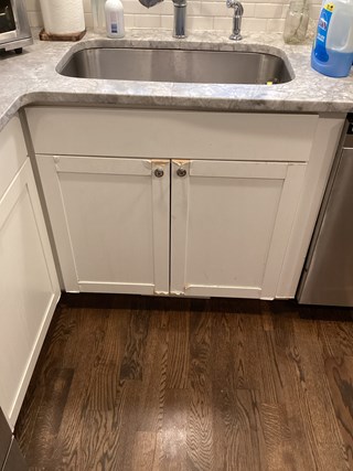 Cabinet doors below the sink are damaged, with noticeable chips and wear around the edges.