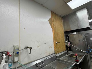 Restaurant kitchen wall wall has visible damage, with the surface peeling and exposing underlying materials.