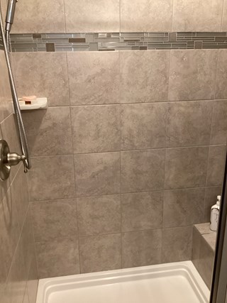 Tile shower with a corner shelf and a bench, but without any additional safety features.