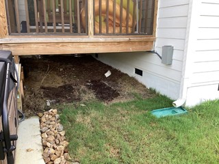 Area beneath a deck with open space, revealing soil and rocks. The area is not enclosed, which could potentially expose it to debris, pests, or the elements.