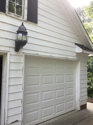 Garage area with the exterior trim and siding in need of attention. The paint is chipped and peeling around the edges, especially near the garage door.