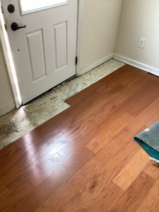 Flooring near the door that is incomplete, with a noticeable gap where some planks are missing.