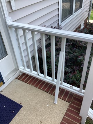 broken section of a porch railing with one of the vertical posts detached and laying on the ground. The damaged railing creates a safety hazard and looks unkempt.