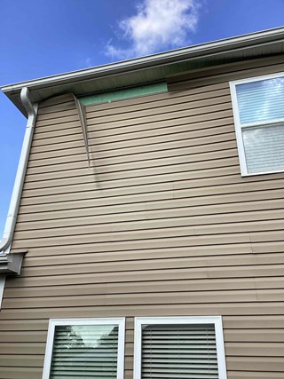 A section of a home's exterior with missing siding at the roofline. 