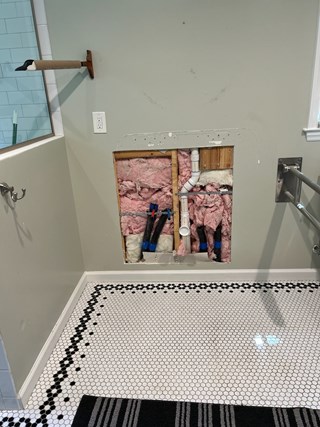 Bathroom with a section of the wall cut out, exposing pipes and insulation during a vanity replacement. 