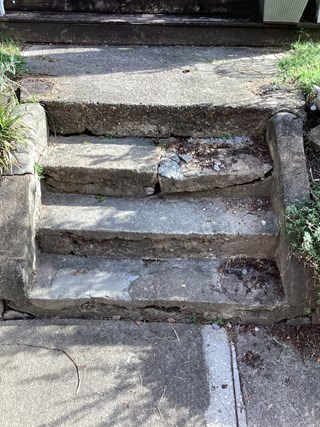 Set of concrete steps that are cracked and damaged, with sections missing and the surface uneven.