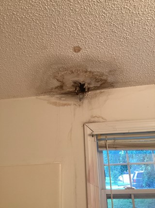Water-damaged ceiling with visible staining and a hole, caused by a leak. 