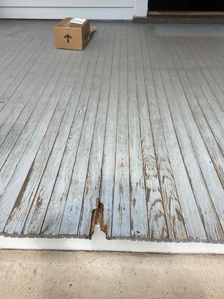 Porch with weathered and damaged wooden boards. One board is visibly cracked and broken,